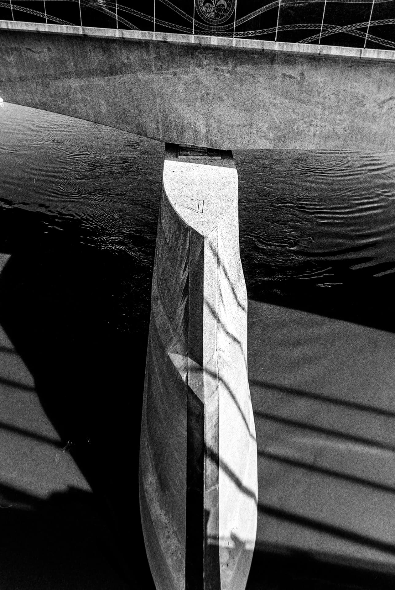 Abstract study of a concrete bridge pier and its shadow over dark water